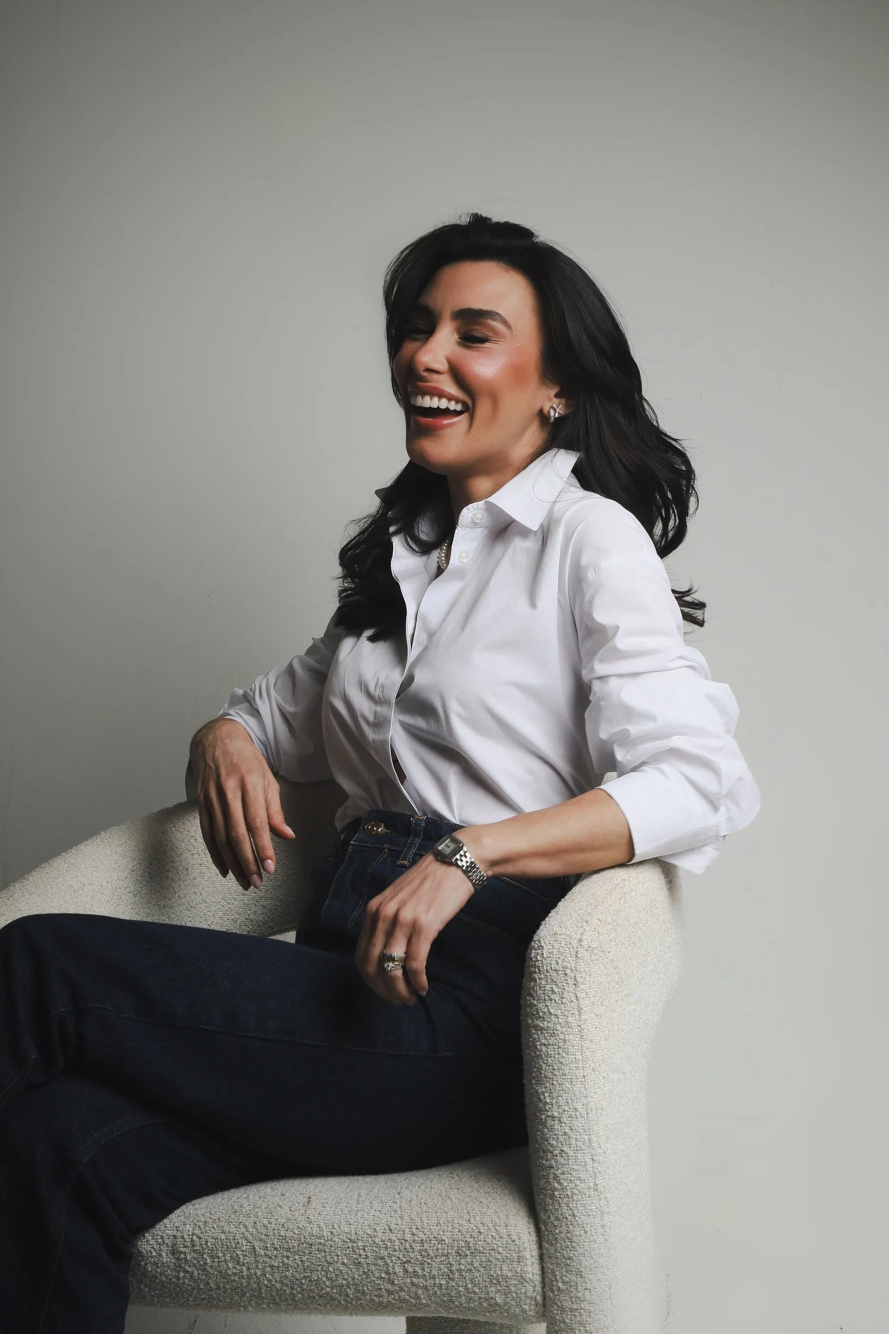 Dra. Ludmila Ramos sorrindo, de camisa branca, sentada numa poltrona